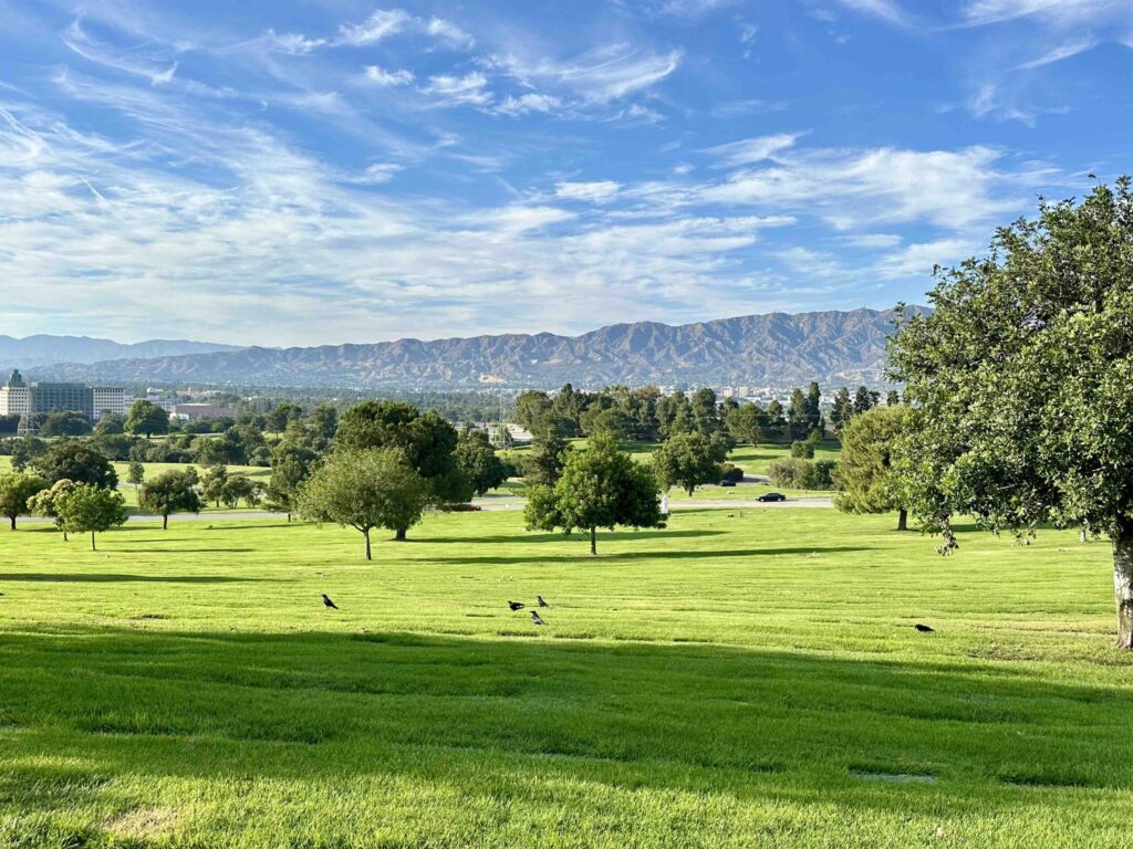 Expansive green lawn at Forest Lawn cemetery leading to distant mountains under a blue sky with scattered clouds, perfect for Feng Shui