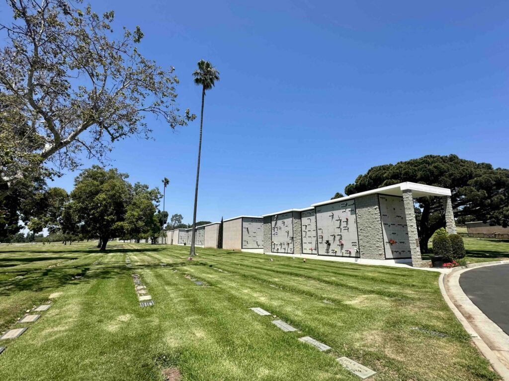 View across Sycamore section on a sunny day with grass, grave markers and Garden of Seasons mausoleum in the background- Bayer Cemetery Brokers